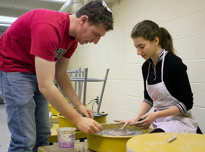 One student guiding another to use a pottery wheel in Studio A